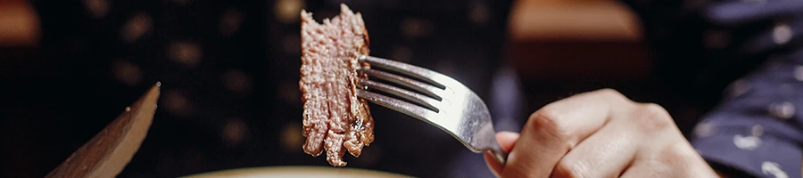 A person holding a piece of steak on a fork