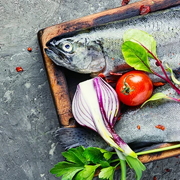 A raw trout with vegetables on a wooden board