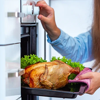 A woman adjusts the temperature of an oven while holding a cooked turkey