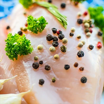 A close up shot of raw rib meat with peppercorns and garnish on top