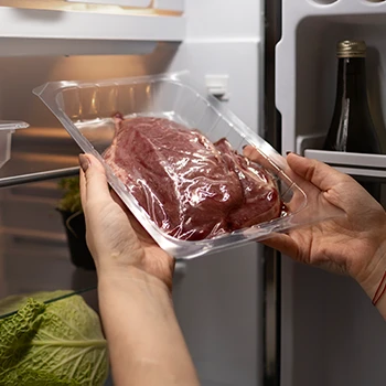 A woman putting a piece of meat in the fridge