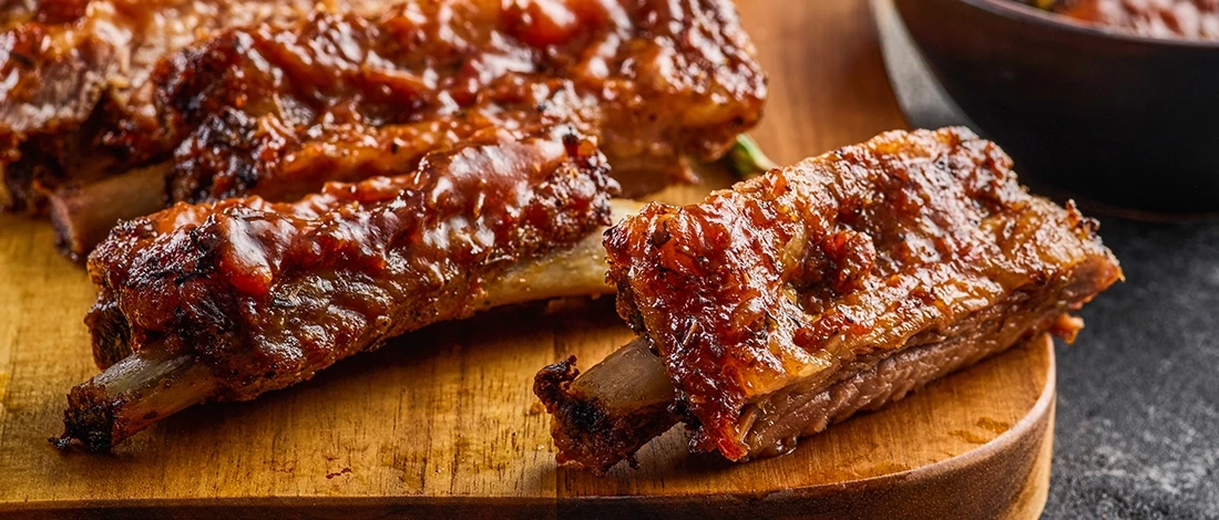 A close up shot of perfectly cooked ribs on a wooden board