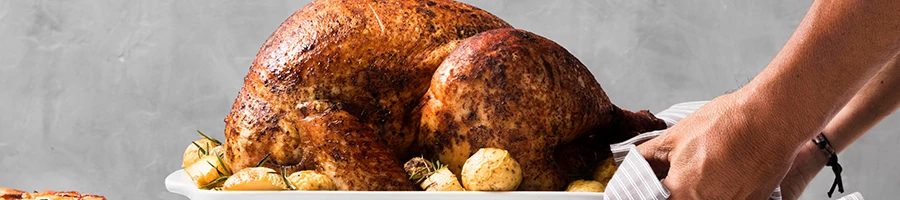 A close up shot of a person placing a roasted turkey on a table