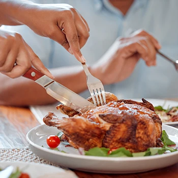 A person slicing a perfectly cooked whole chicken on a table