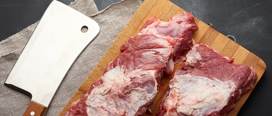 A top view of meat on a cutting board with a butcher knife on the side