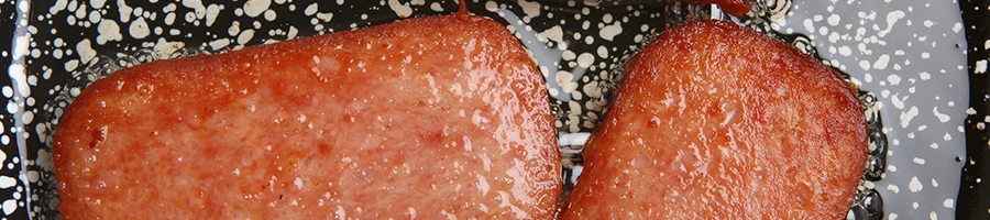 A top view of spam meat being fried on a non-stick pan