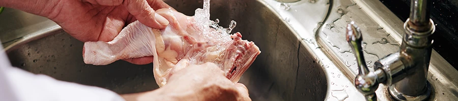 A person washing raw chicken meat in the sink