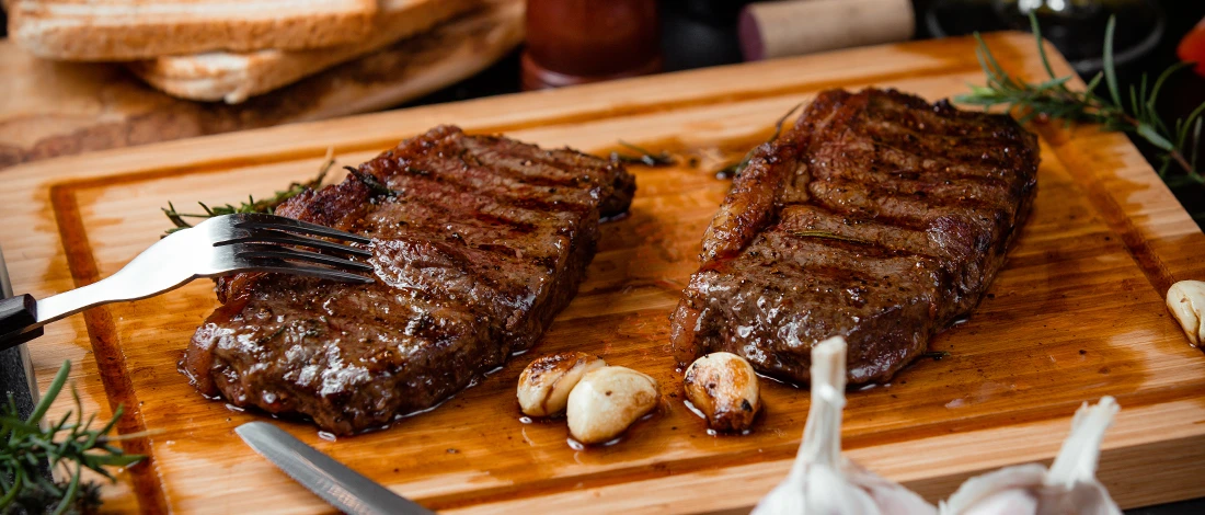 Two pieces of steak resting on top of a wooden board