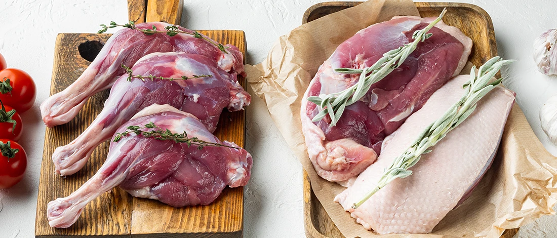 Different cuts of raw duck meat on top of a wooden board