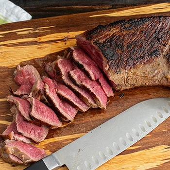 A wooden board with roasted tri-tip beef as a brisket substitute