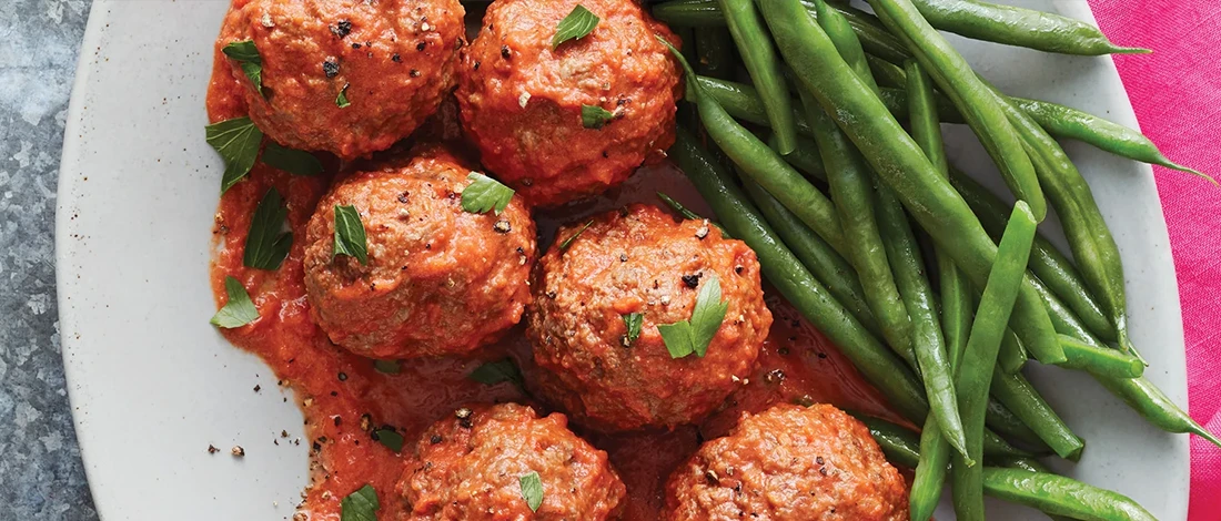 A top view of meatballs with vodka sauce and vegetables