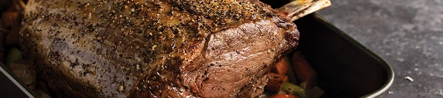 A cooked prime rib on a cooking pan with vegetables