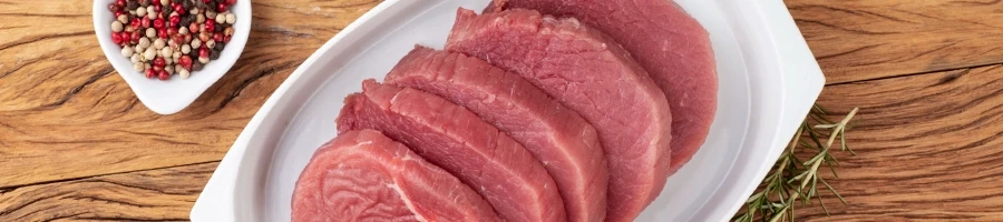 Raw eye of round steak on a white plate ready to be tenderized