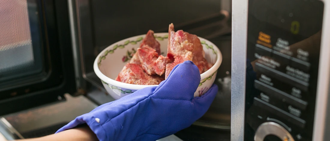 A person defrosting meat using a microwave