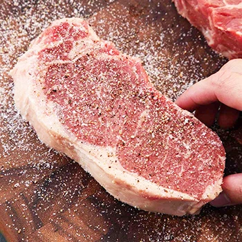 A raw steak being seasoned perfectly