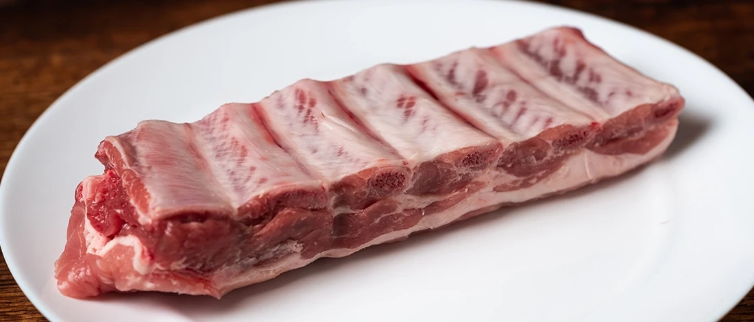 Raw pork ribs on a white plate ready to be stored in the fridge