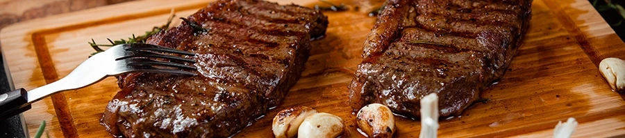 Two reheated steaks on top of a wooden board