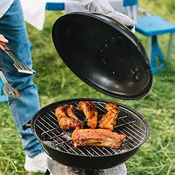 a photo of a charcoal grill with a person holding the lid