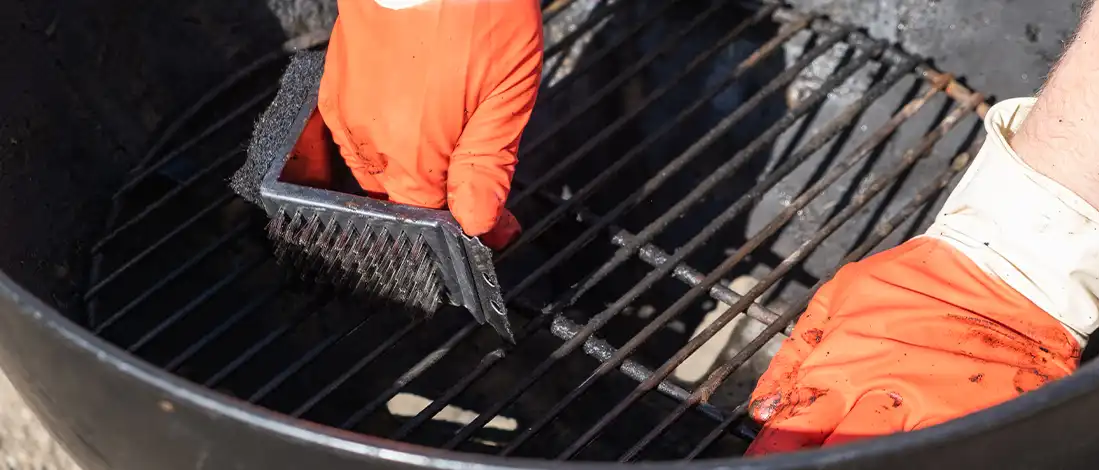 a person with orange gloves cleaning charcoal grill