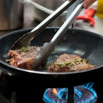 A person cooking steak in a pan