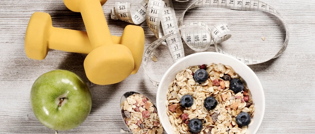 A top view of oatmeal on a bowl with berries, an apple, a tape measure, and dumbbells