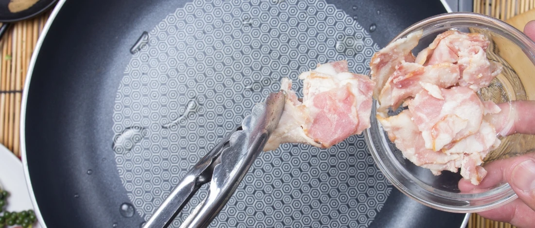 A person putting meat on a pan