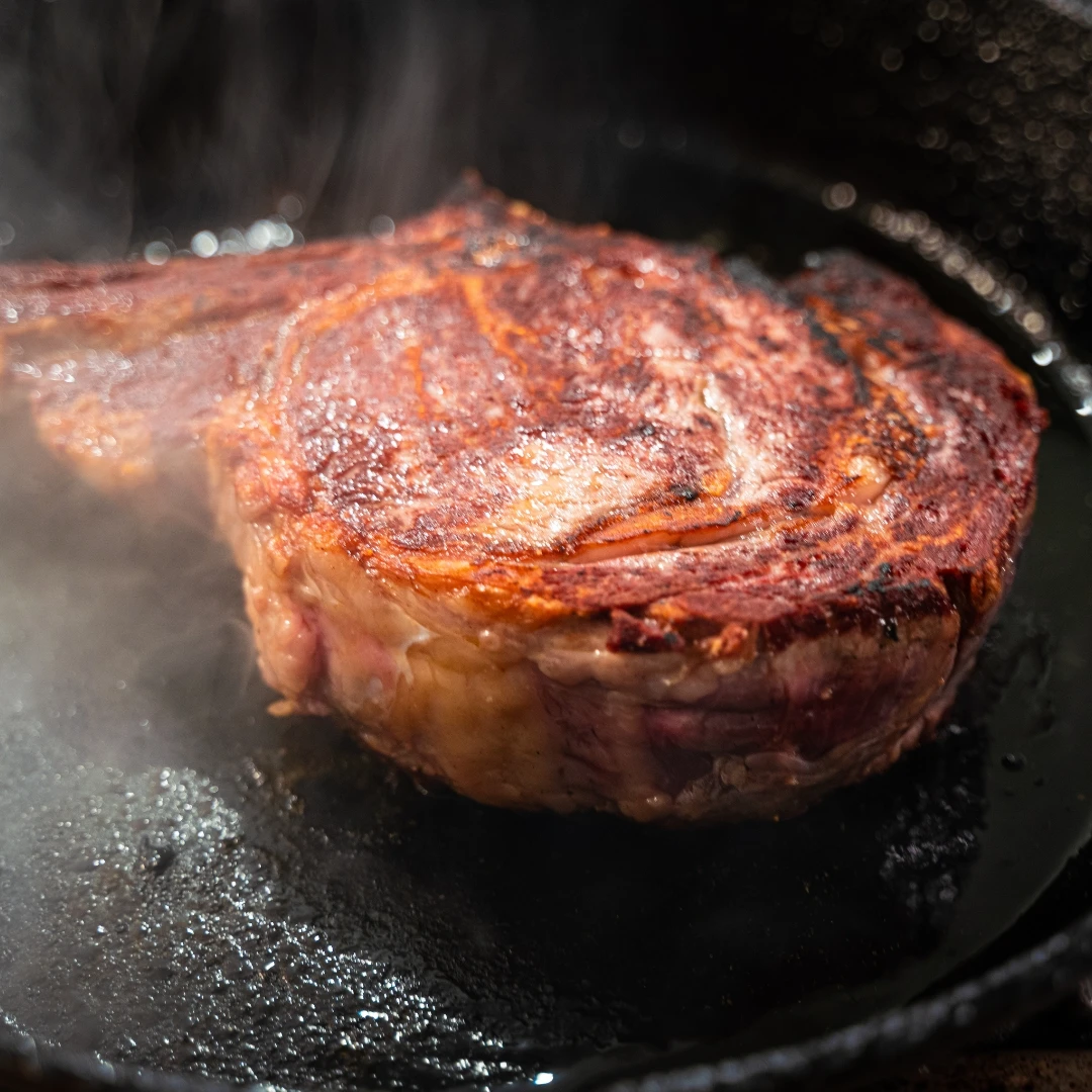 A Bison steak cooking on a pan