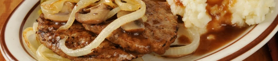 A plate of steak with onions and mashed potatoes